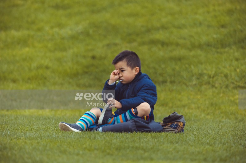 Boy sitting in field rubbing eye