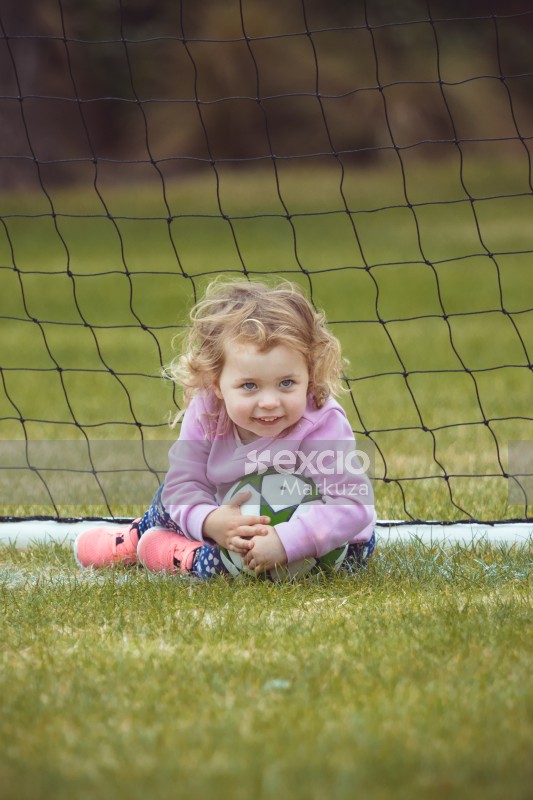 Grey eyed girl holding onto a football - Little Dribblers