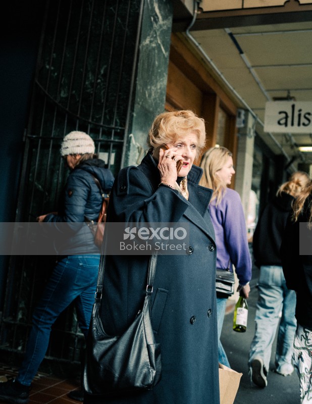 Elderly lady on phone in a black long coat and black purse