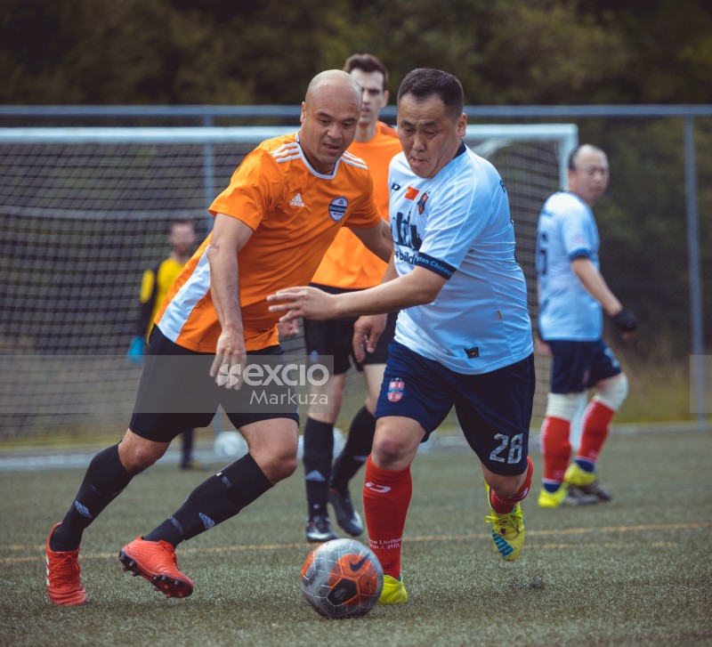 Bald and Asian players compete to gain possesion of football - Sports Zone sunday league