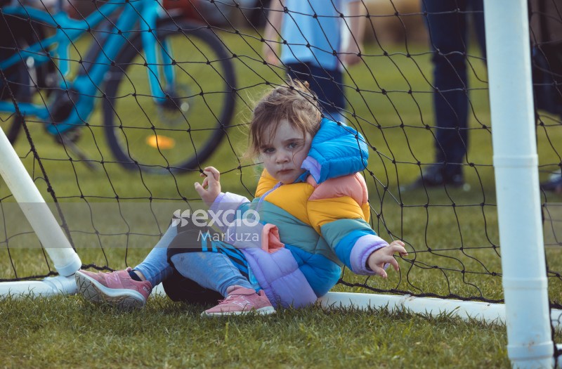 Little girl sitting inside goal post at Little Dribblers football match