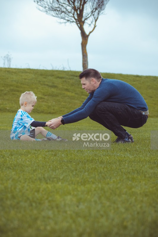 Father and son wearing blue shirts sitting on grass