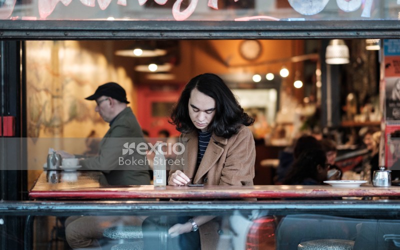 A woman in brown coat looking at her phone in a cafe