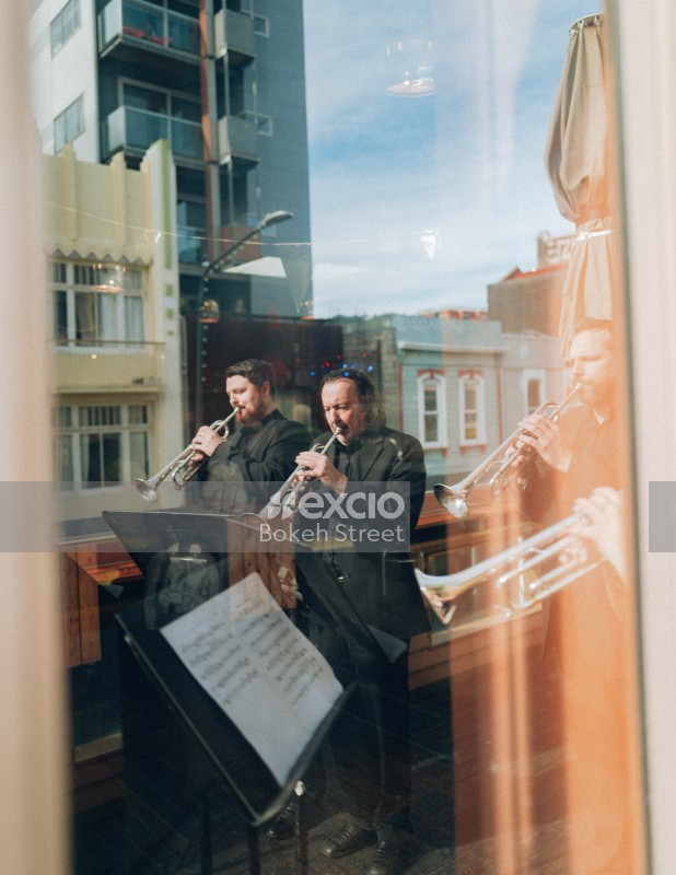 Reflection of musicians playing trumpets buildings and sky on glass