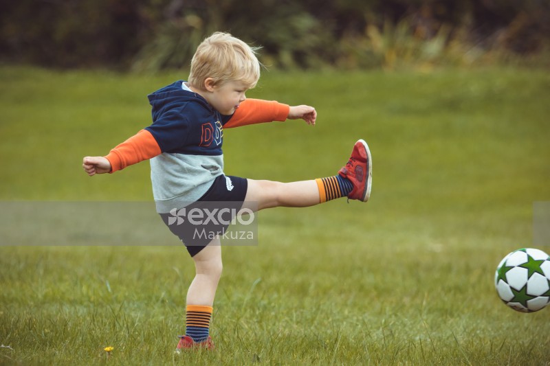 Kid wearing striped socks and red shoes kicking football - Little Dribblers