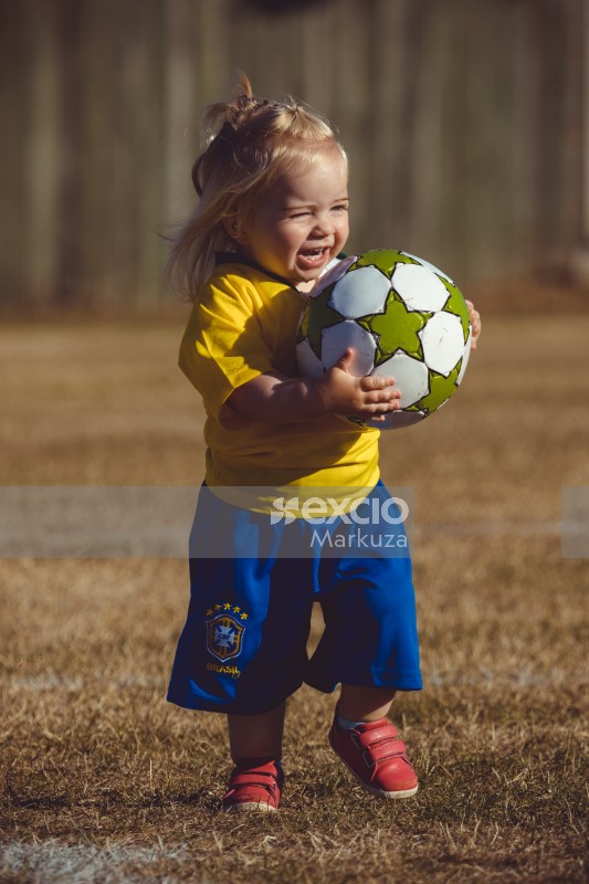 Excited little girl in Brasil kit carrying a football - Little Dribblers