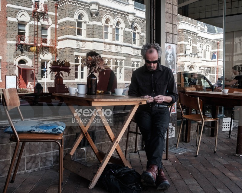 Man in black clothes sitting outside a cafe having coffee