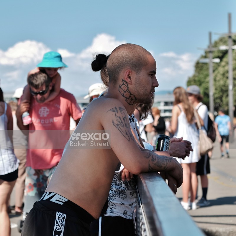 Shirtless guy with tattoos leaning on a railing at an event in Wellington
