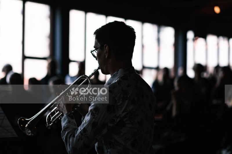 Guy playing trumpet at a classical concert wearing glasses and floral shirt