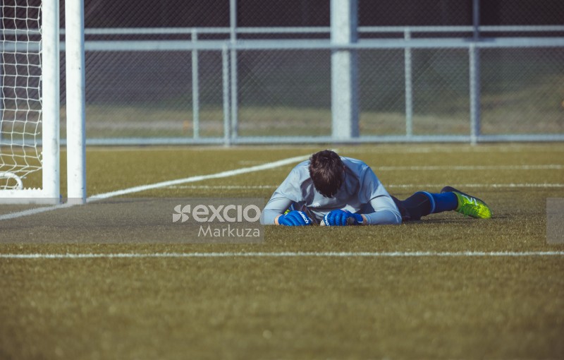 Goalkeeper wearing blue gloves lying down on grass - Sports Zone sunday league