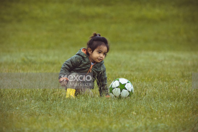 Little girl sitting in grass with a football - Little Dribblers