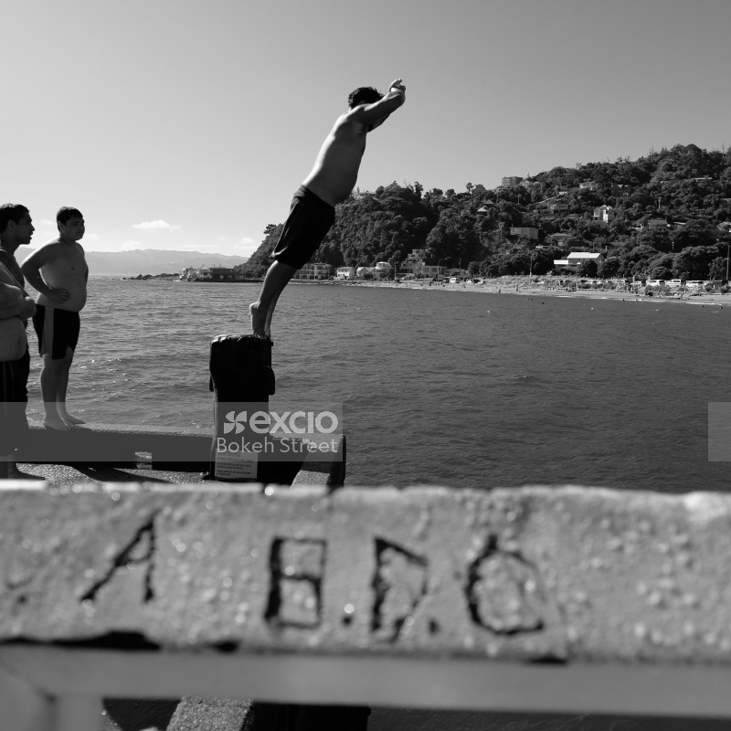  Boy diving from a platform on wharf into the water in Days bay monochrome