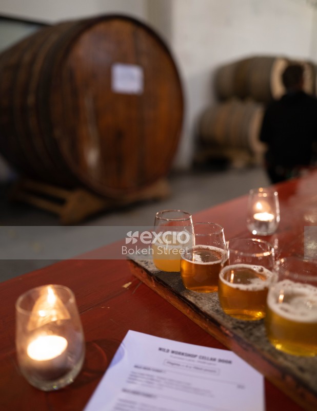 Four beer glasses and candles on a table next to a barrel