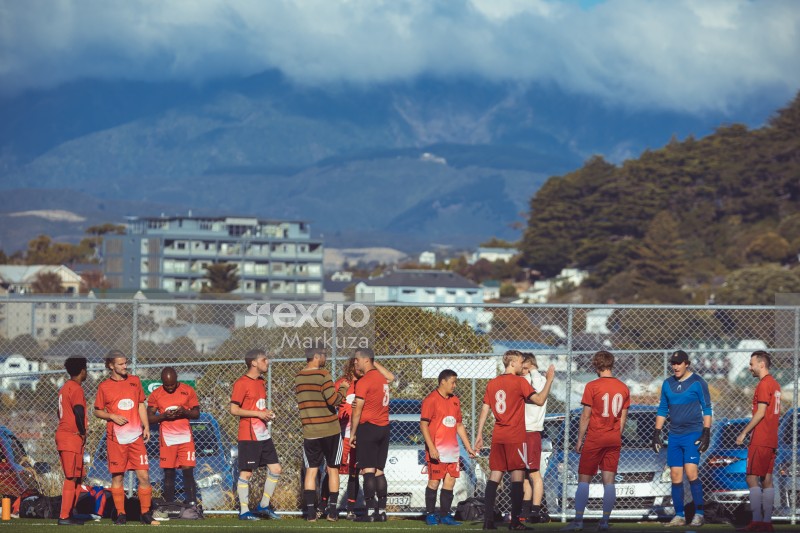 Players on the sidelines by the fence and mountains in the backdrop - Sports Zone sunday league