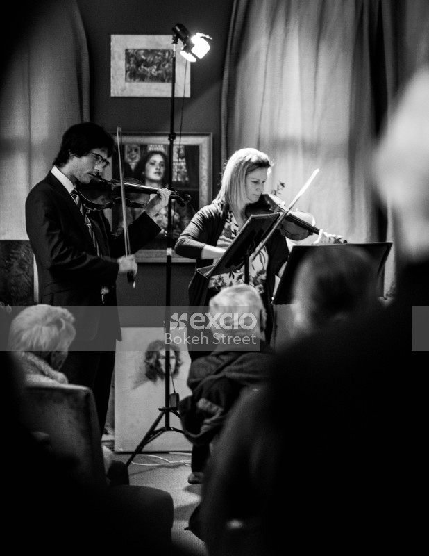 People playing violin at a classical concert with paintings black and white