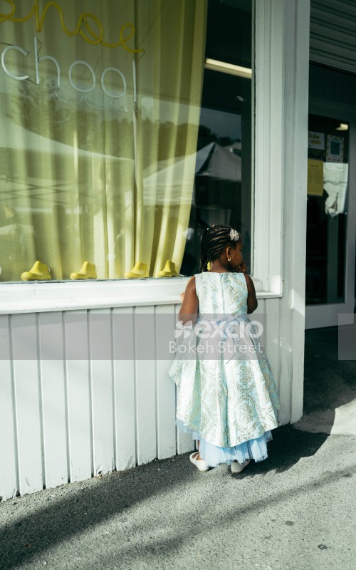 Little girl with cornrows and white dress looking through a shop window at Newtown festival 2021