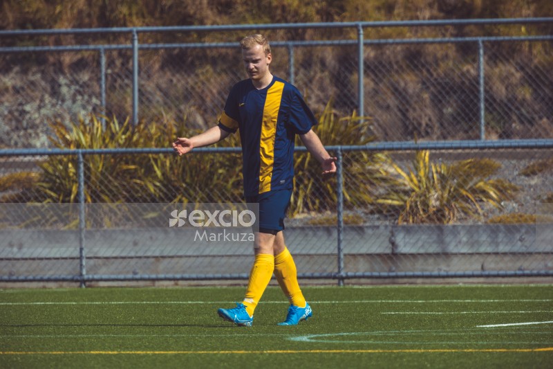 Football player in blue and yellow kit walking on field - Sports Zone sunday league