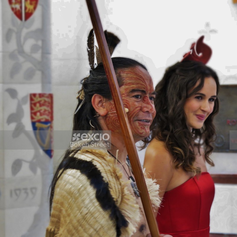 Man in traditional Maori attire tattoos and woman in red dress