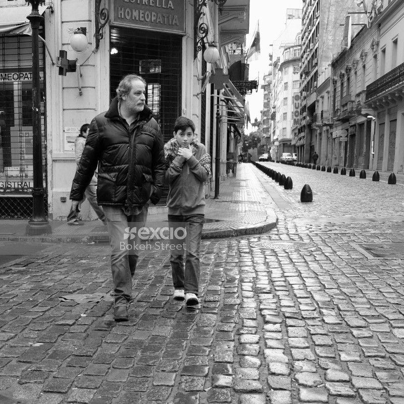 Father and son walking on cobbled street winter black and white