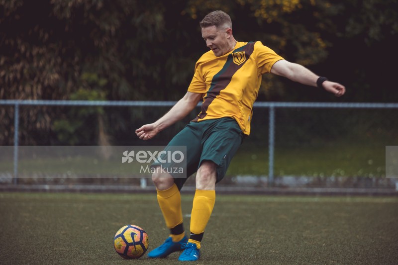 Player in yellow shirt and blue cleats kicking a football - Sports Zone sunday league