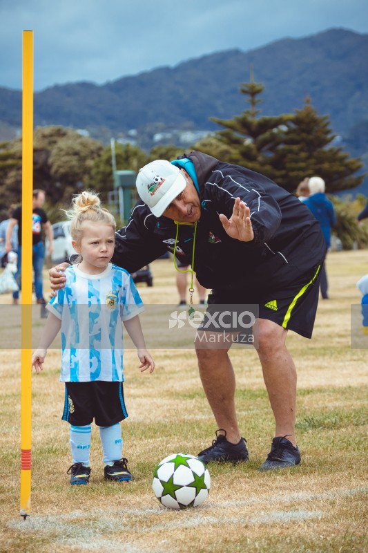 Coach guiding little girl in Argentine kit where to kick football