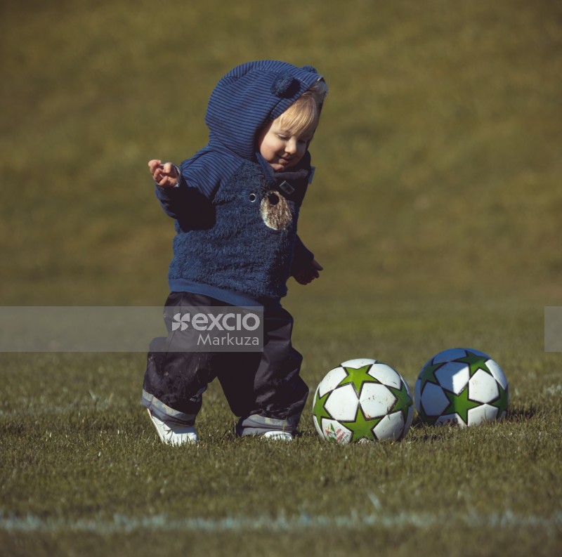 Little kid in blue hoodie kicking a football