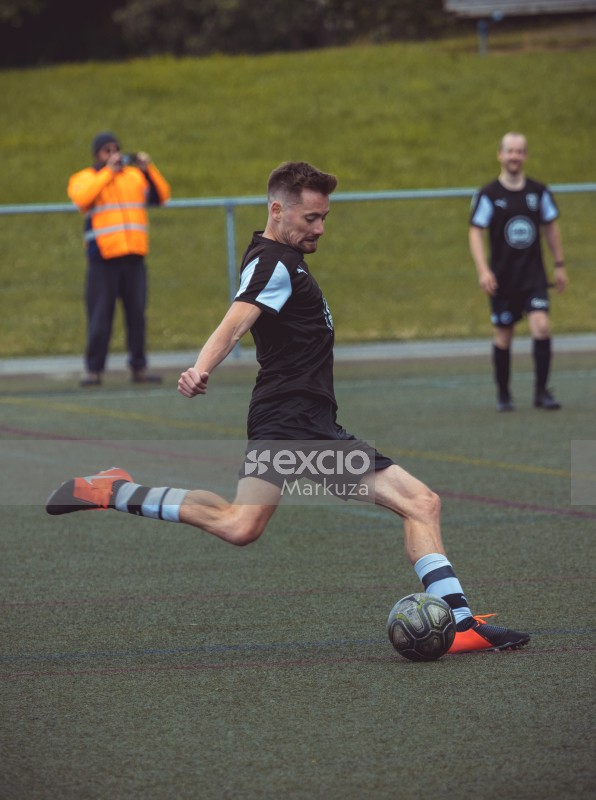 Player wearing black and orange cleats kicking football - Sports Zone sunday league