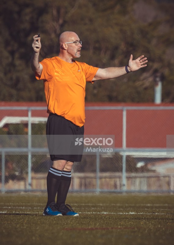 Referee holding whistle spreads both arms in the air - Sports Zone sunday league