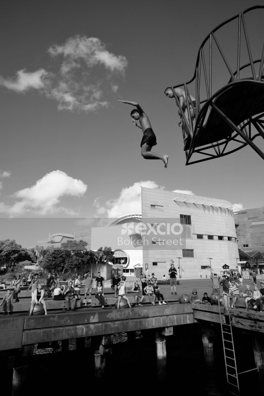 Boys jumping into the water from a diving platform black and white