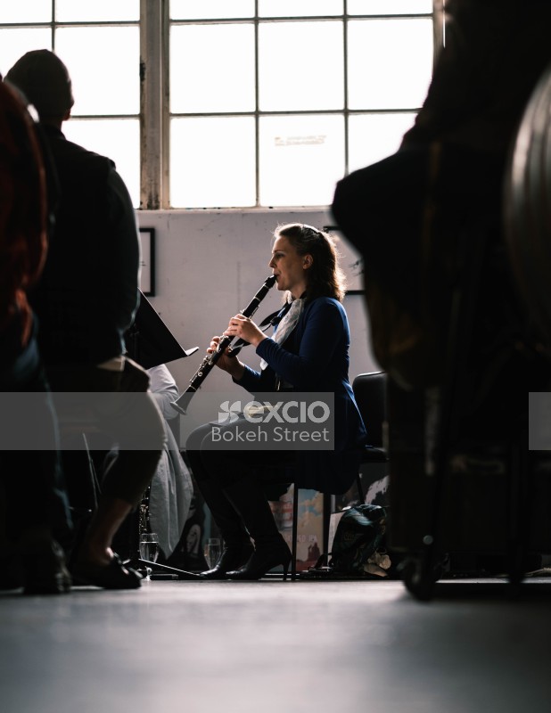 Woman playing clarinet in a concert wearing blue shirt and a white scarf sitting on a chair