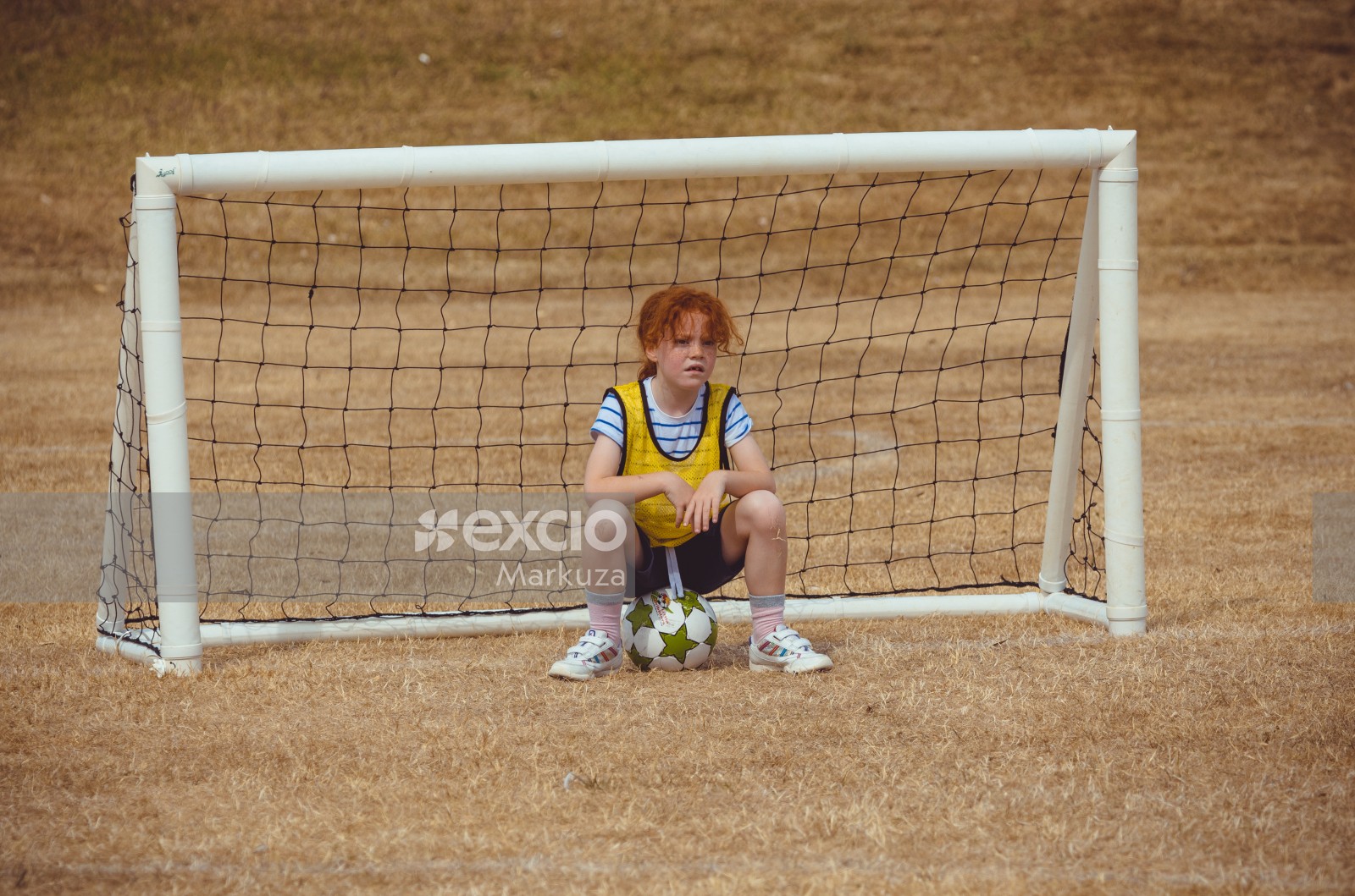 Girl in yellow scrimmage vest sitting on a football - Little Dribblers