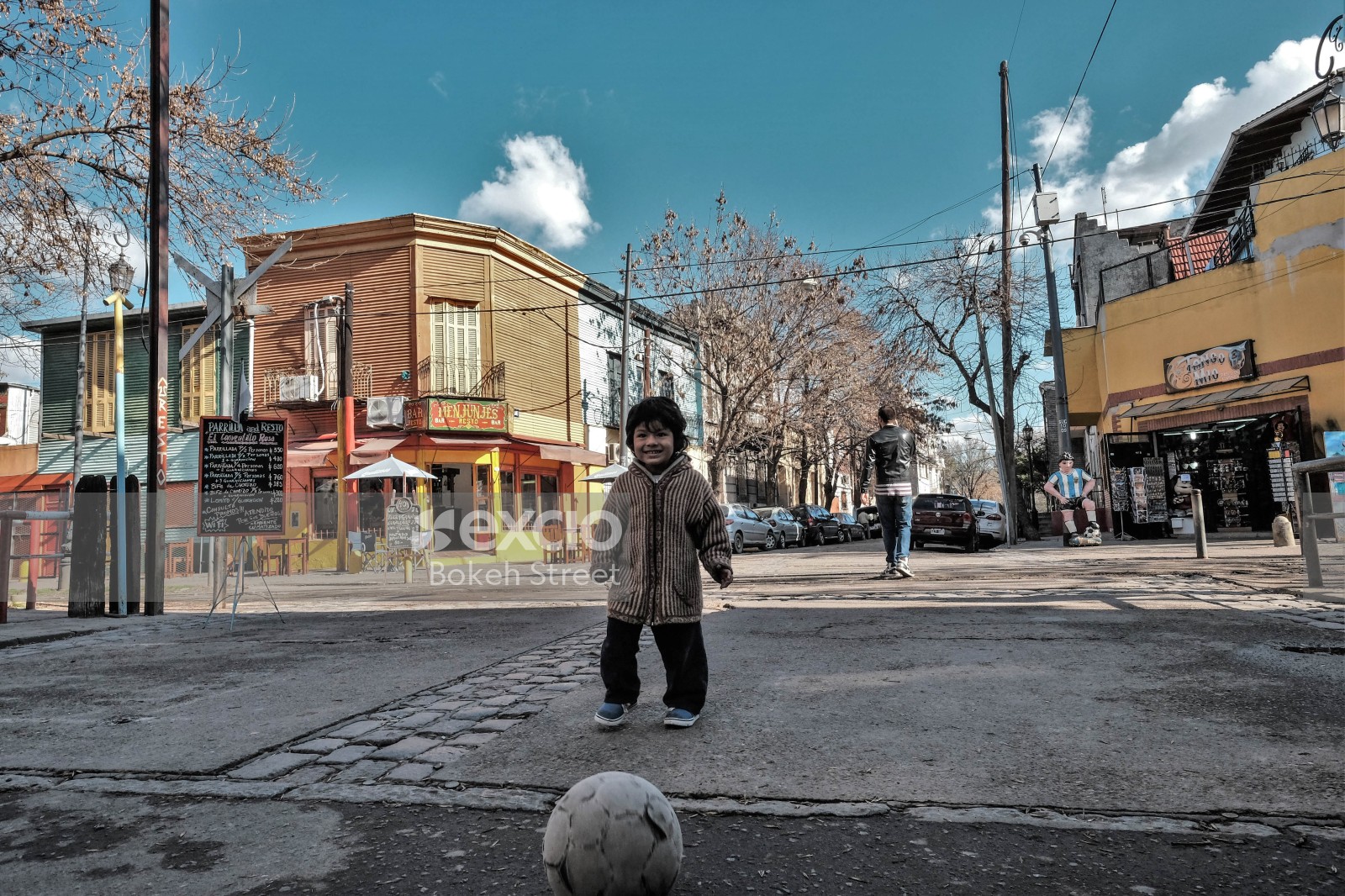 Kid playing football in the street Maradona statue