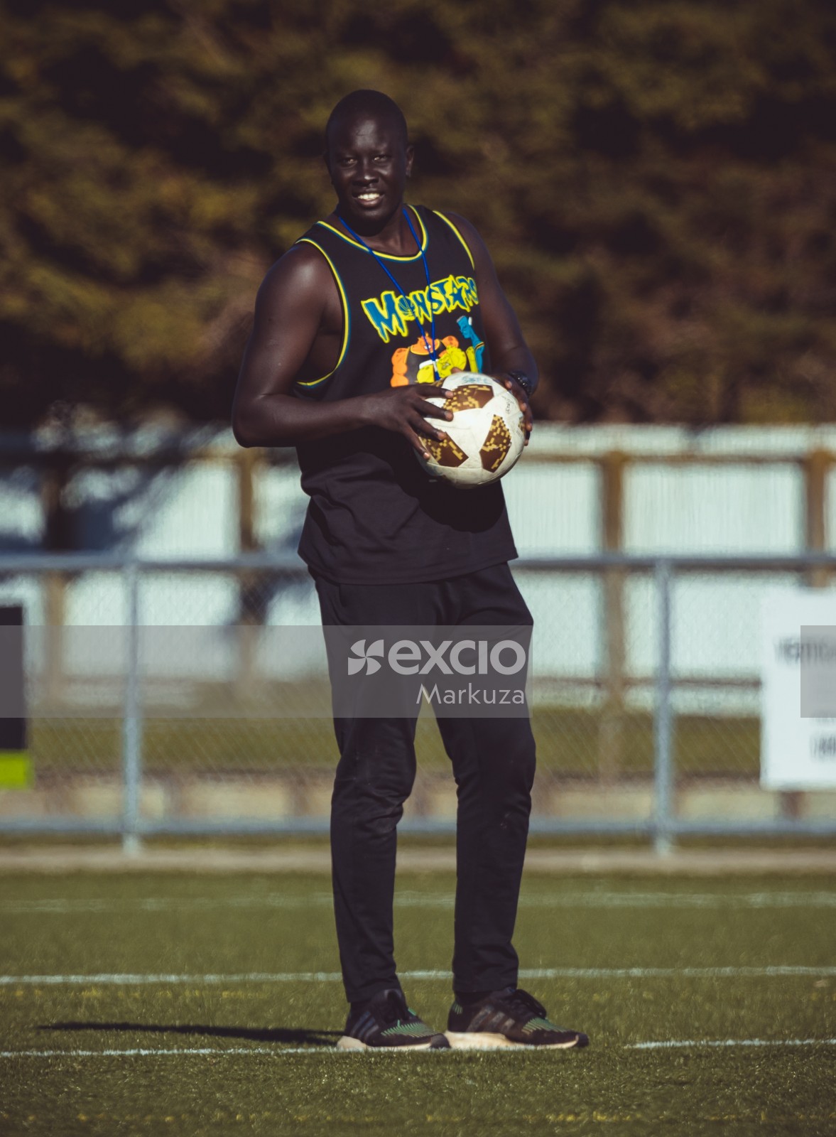 Dark skinned guy in a black tank top holding football - Sports Zone sunday league