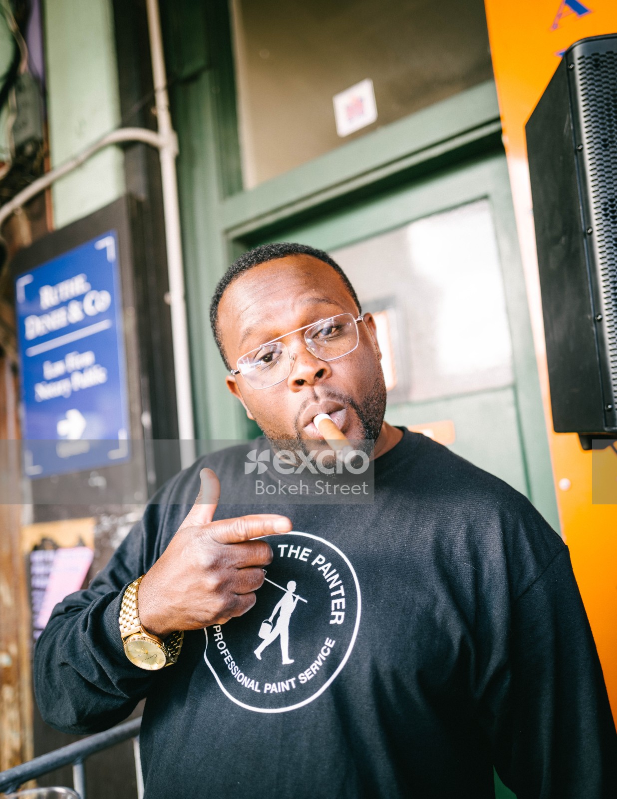Dark skinned man with a golden watch smoking a cigar at Newtown festival 2021