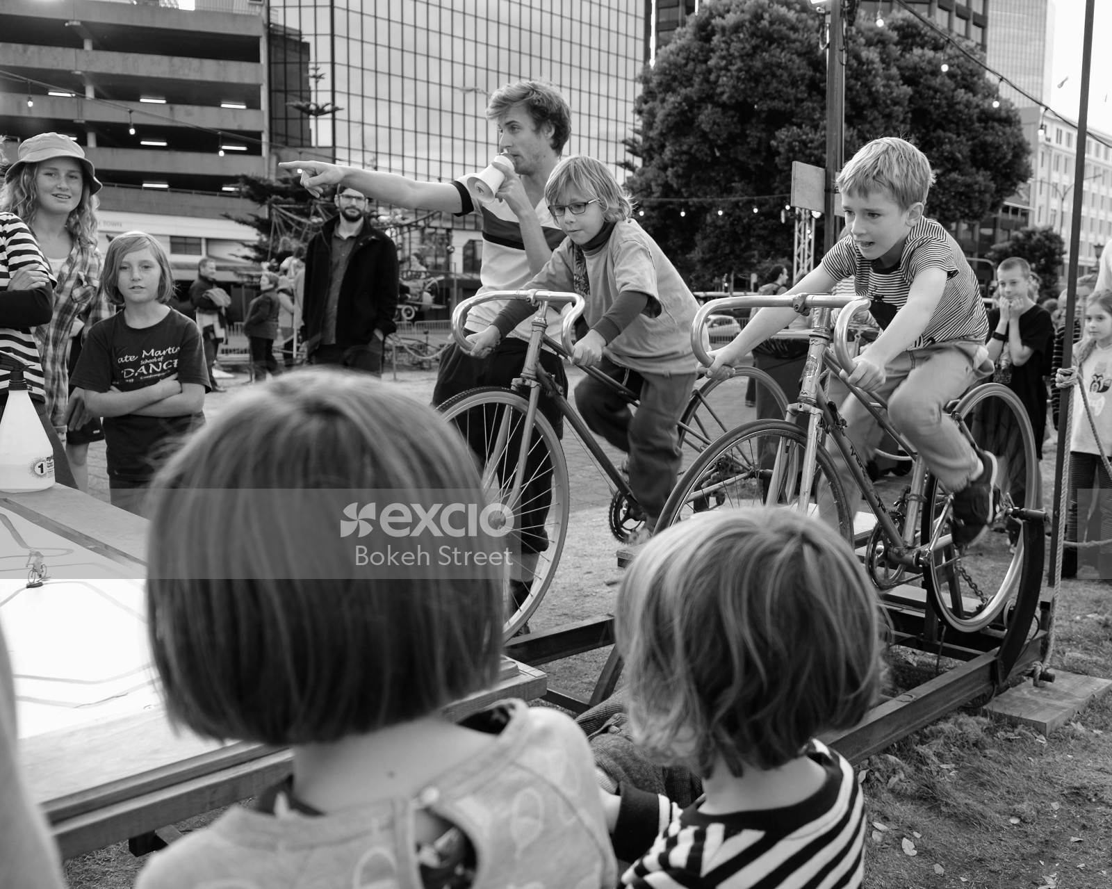 Children racing a stationary cycle at a festival black and white
