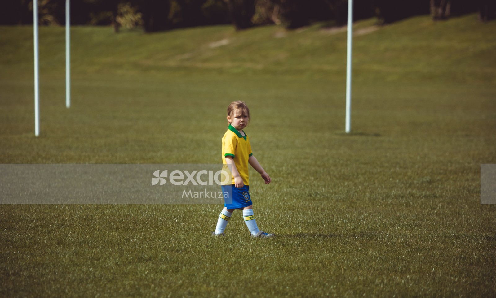 Little girl in Brasil football team uniform walking on grass - Little Dribblers