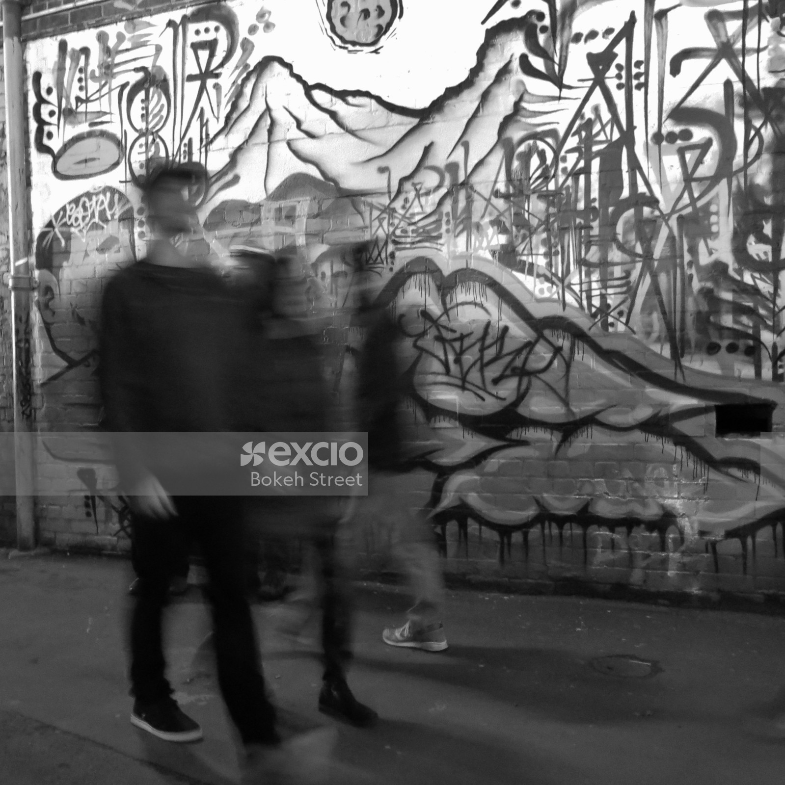 People walking by a graffitied wall black and white long exposure