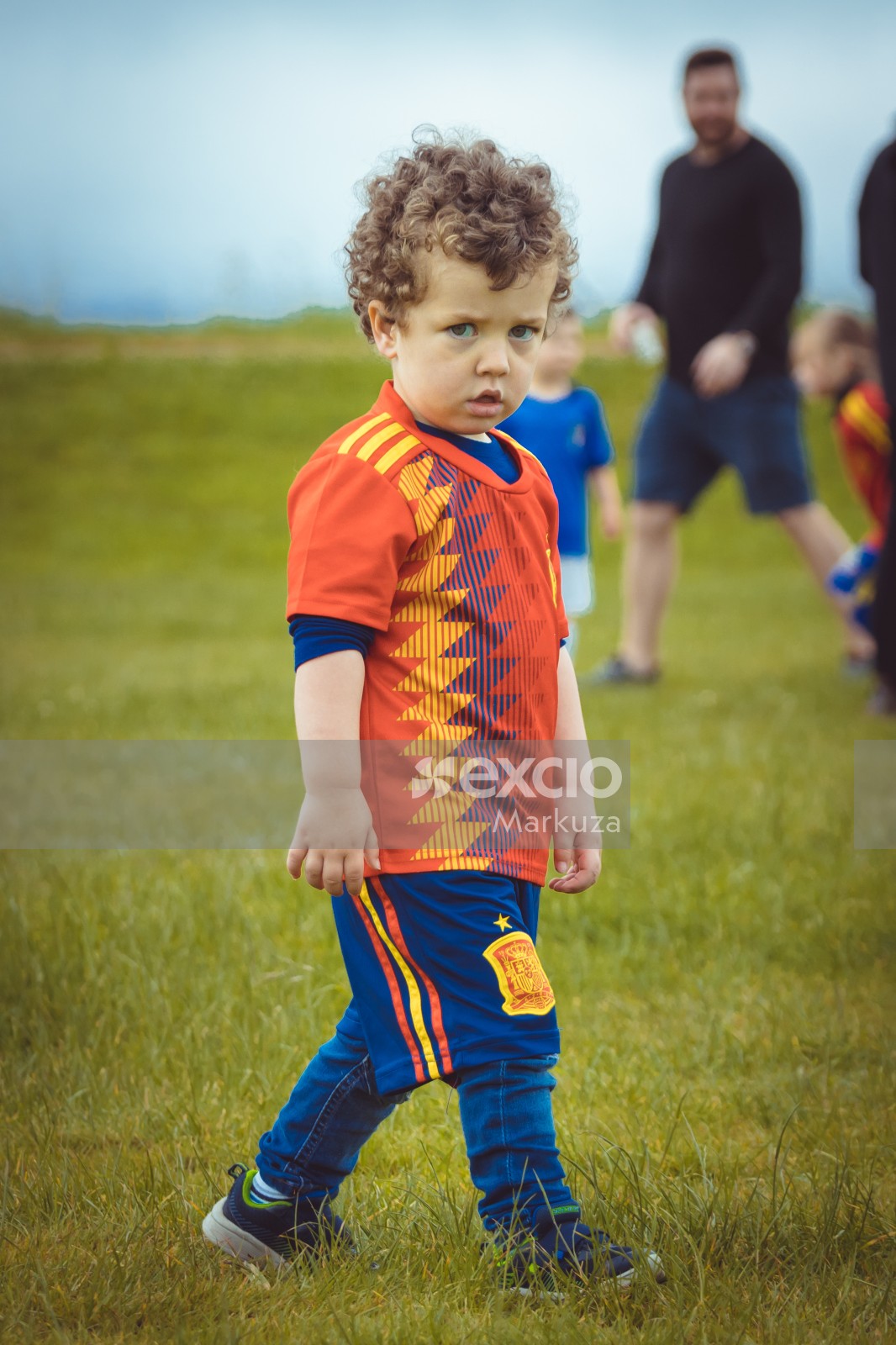 Curly haired boy in Manchester United kit walking on grass - Little Dribblers