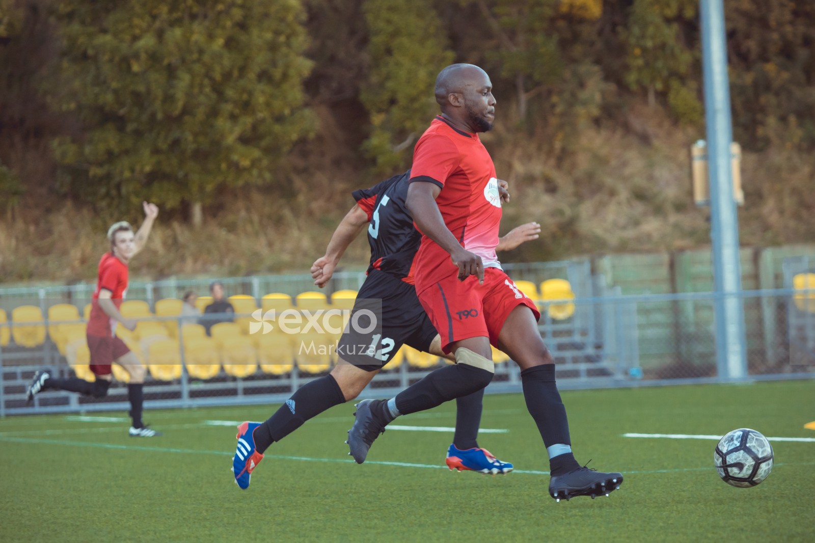 Bald dark skinned player in red shirt playing football - Sports Zone sunday league
