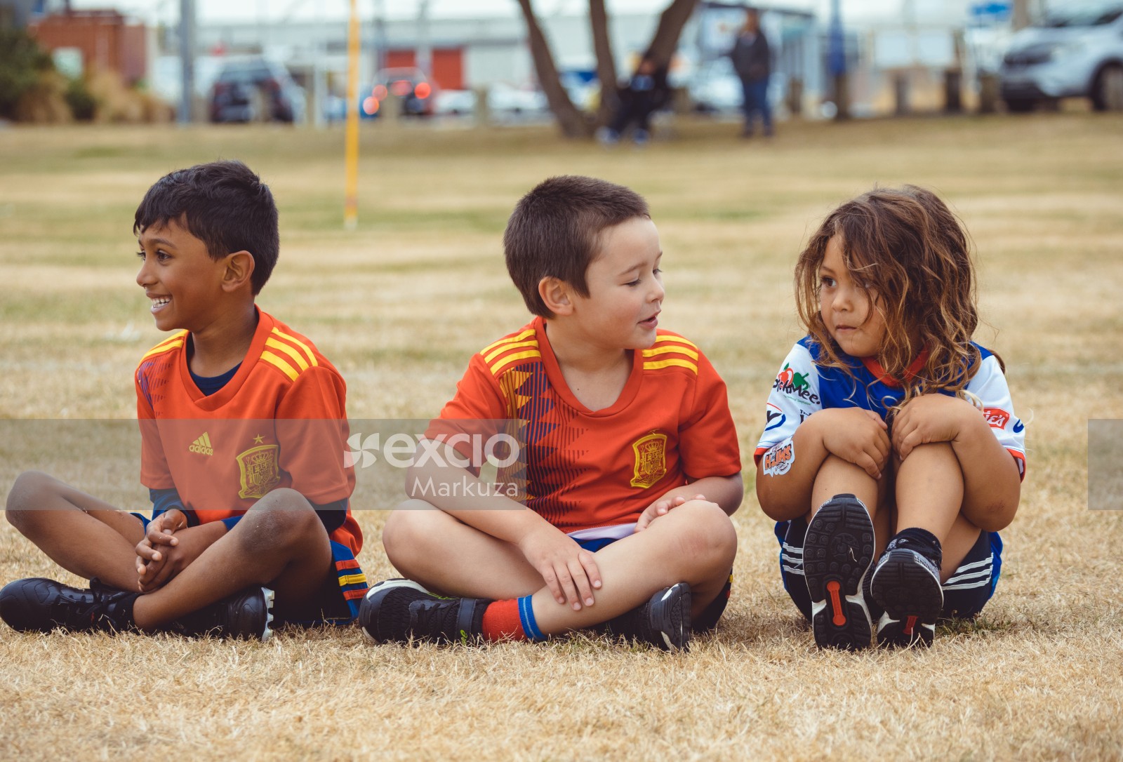 Children sitting on dry grass at Little Dribblers sports play