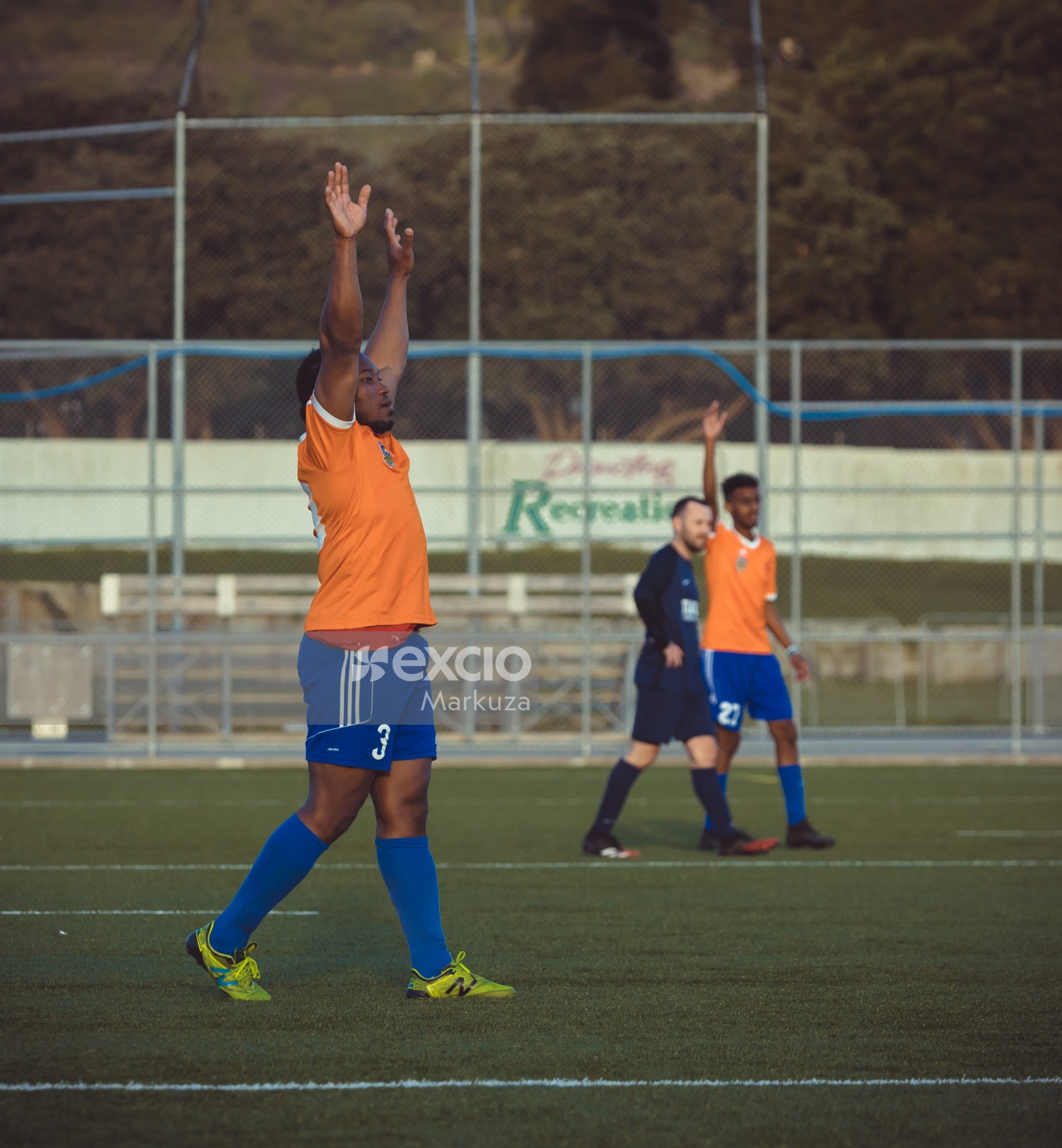Player in orange Adidas shirt raising both hands - Sports Zone sunday league