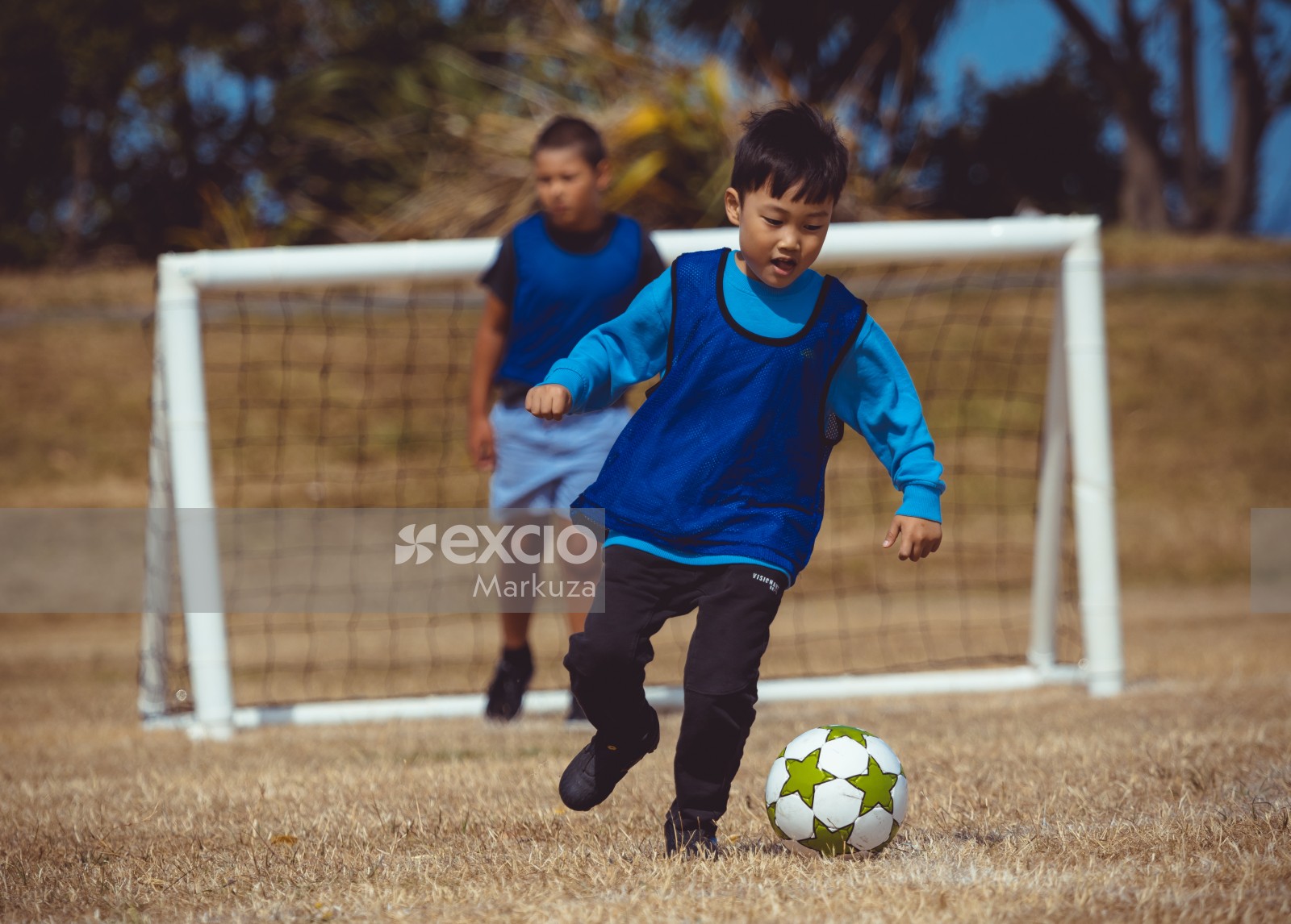 Boy in blue shirt and scrimmage vest playing football - Little Dribblers