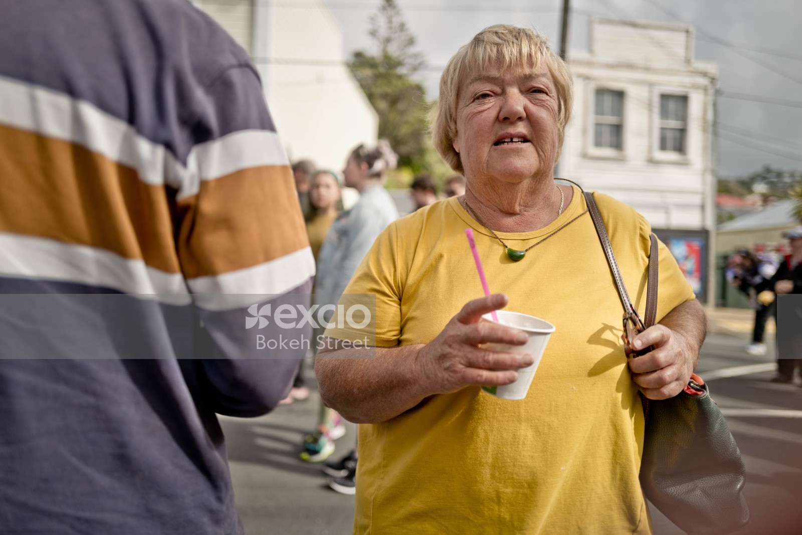 Old lady wearing a yellow shirt holding a cup at Newtown festival 2021