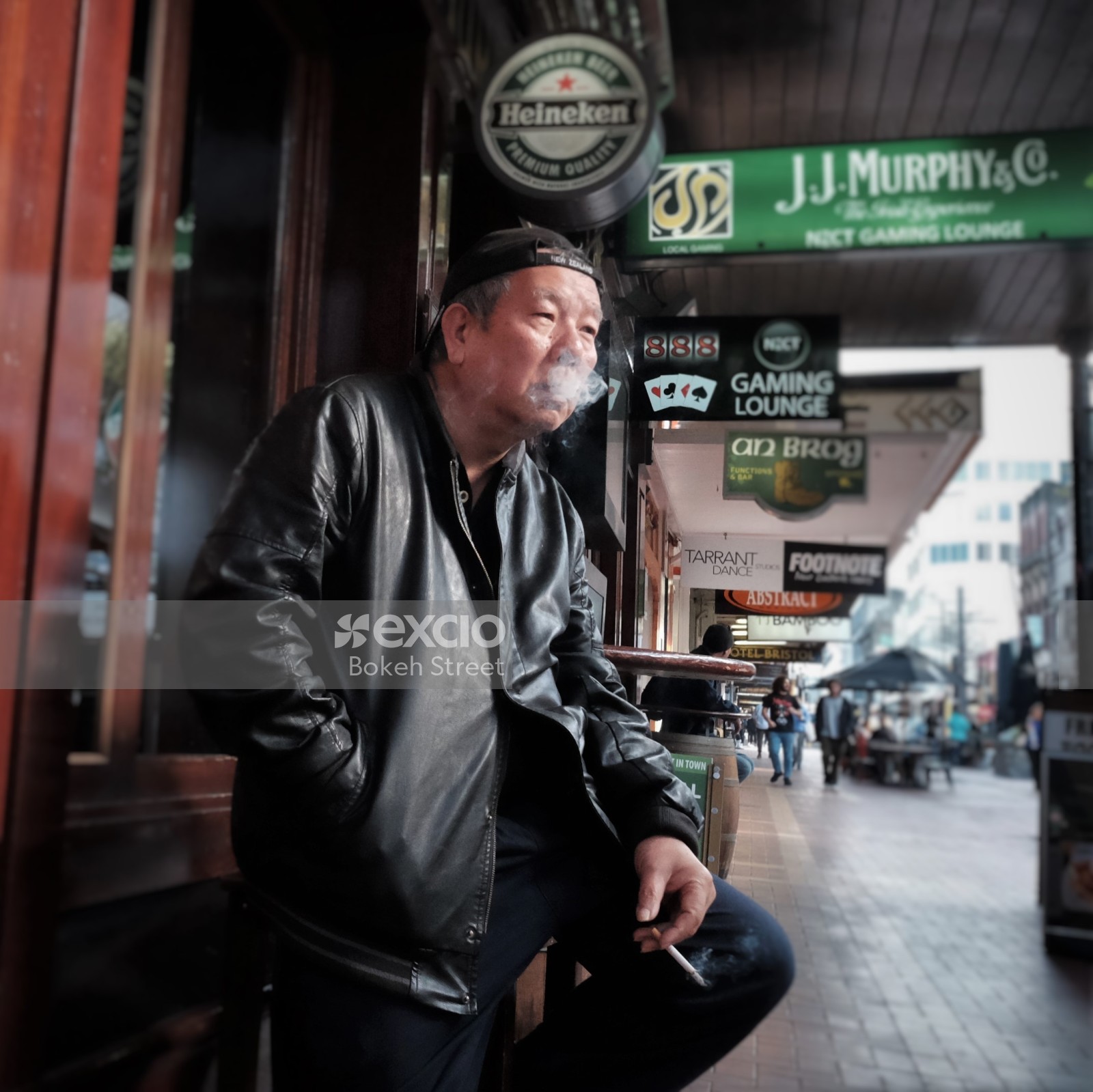 Old man in a leather jacket and reverse cap smoking a cigarette in the street