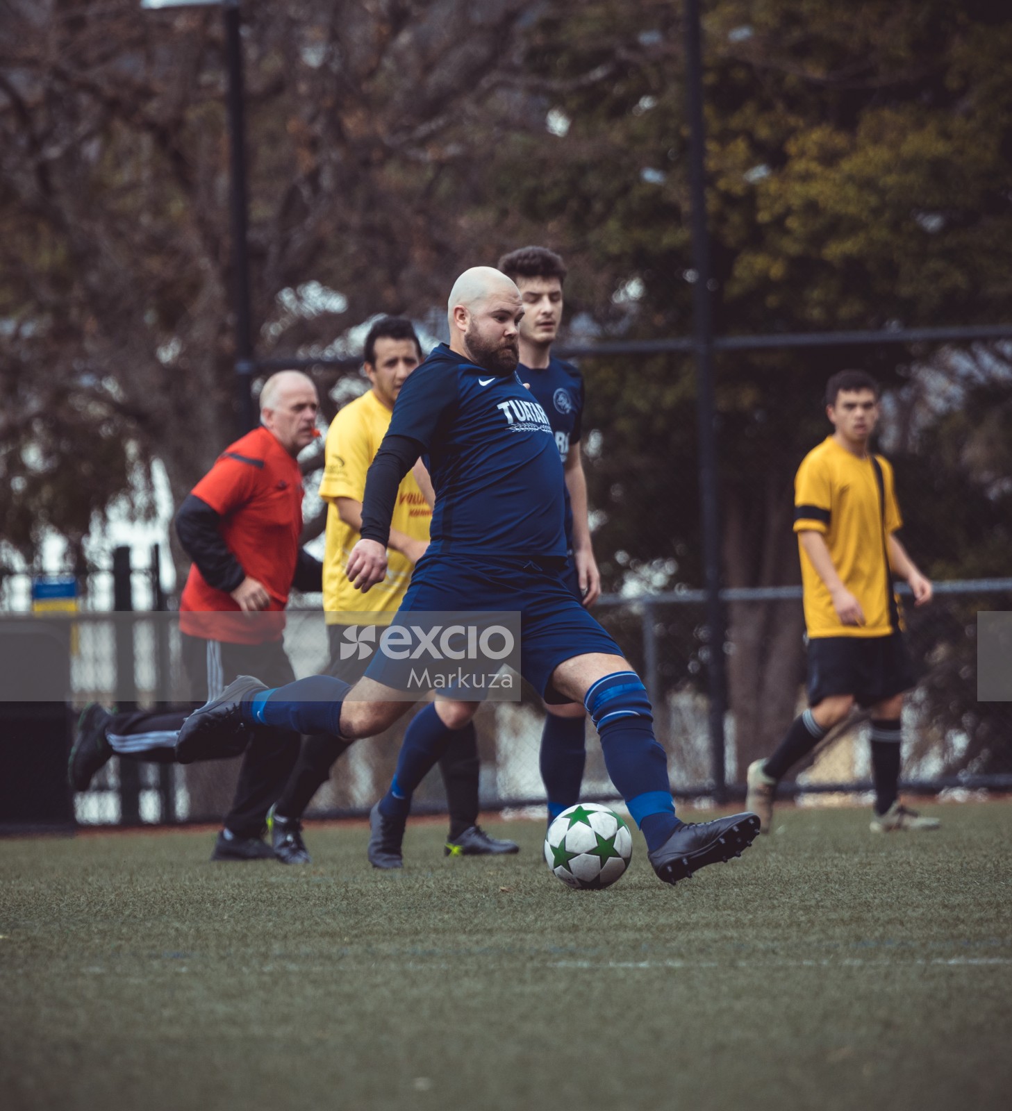 Bald and bearded football player in blue kit kicks ball - Sports Zone sunday league