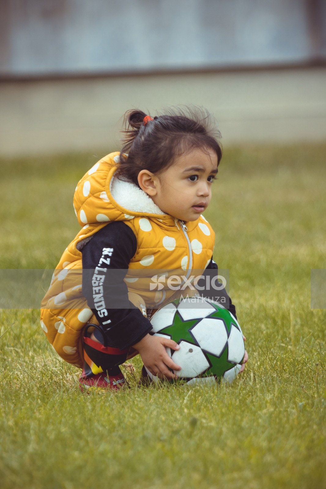Girl in yellow polka dot jacket sitting on the grass - Little Dribblers