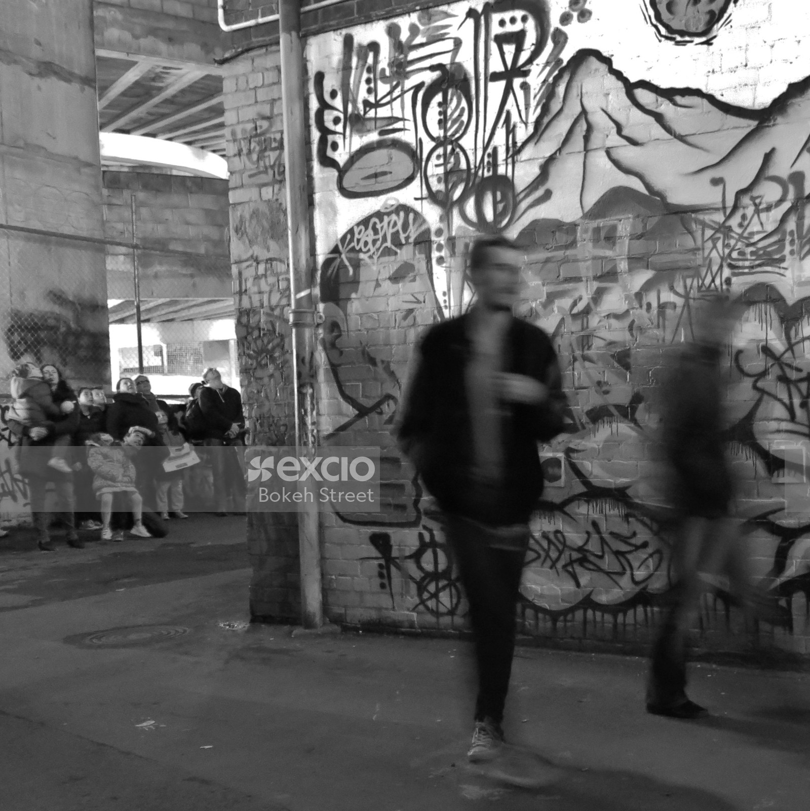 People around a graffitied wall long exposure monochrome