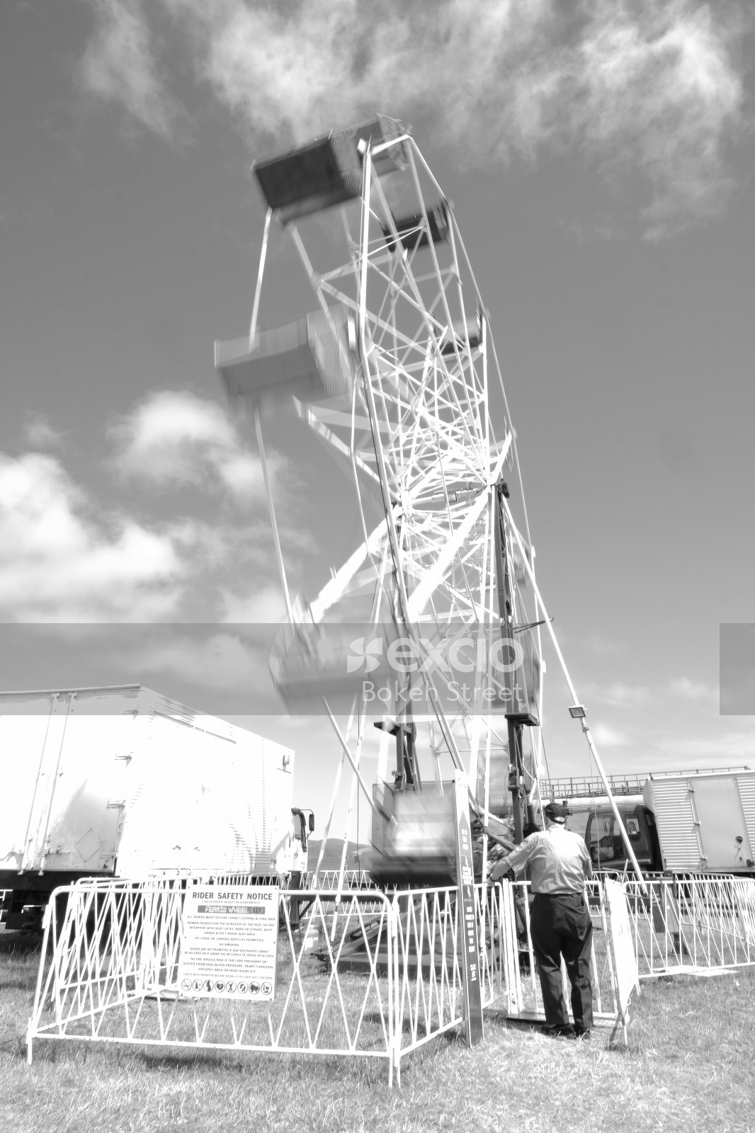 Operator standing next to ferris wheel at a carnival black and white