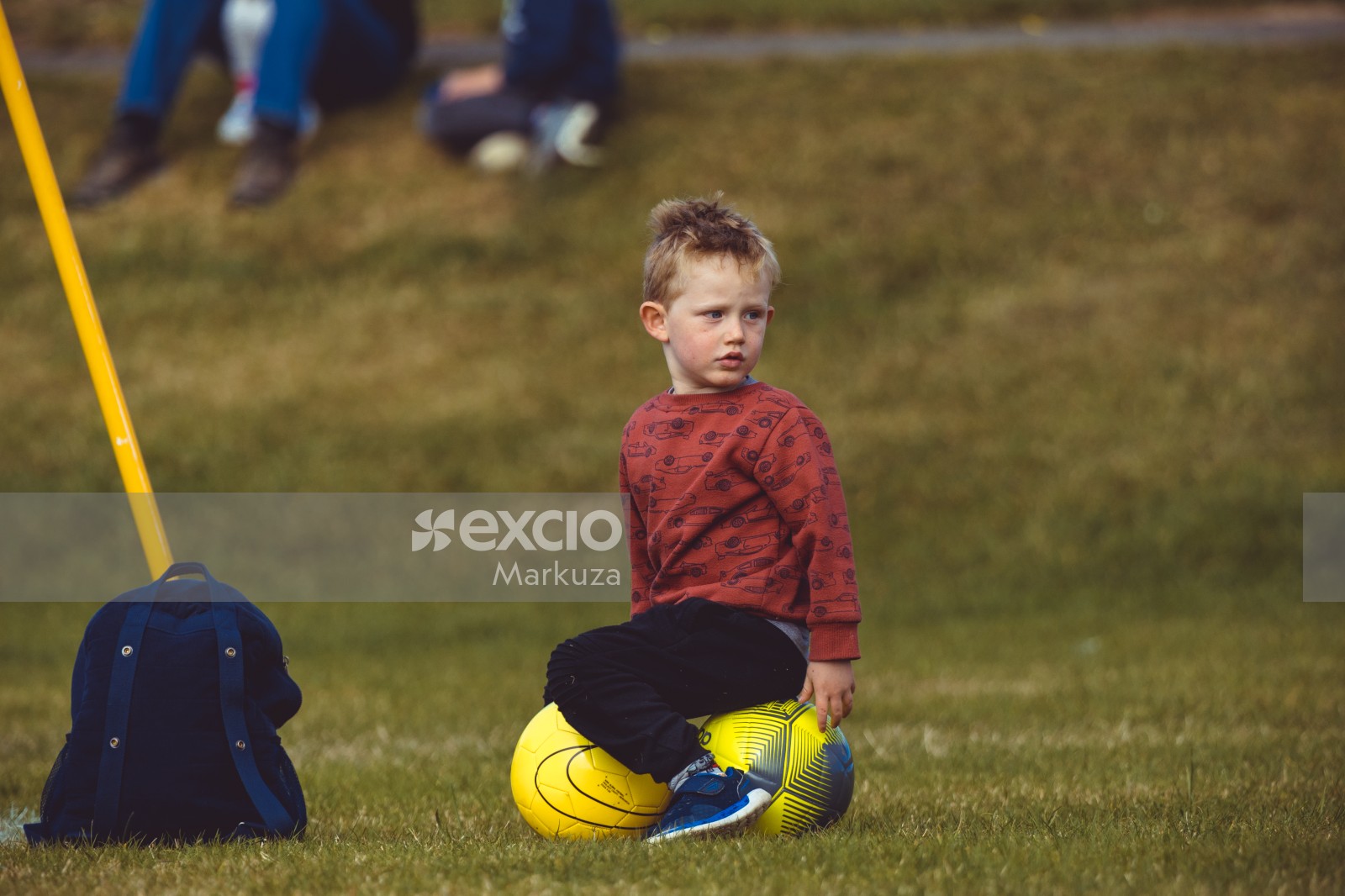 Little boy in red shirt sitting on footballs at Little Dribblers soccer exhibition