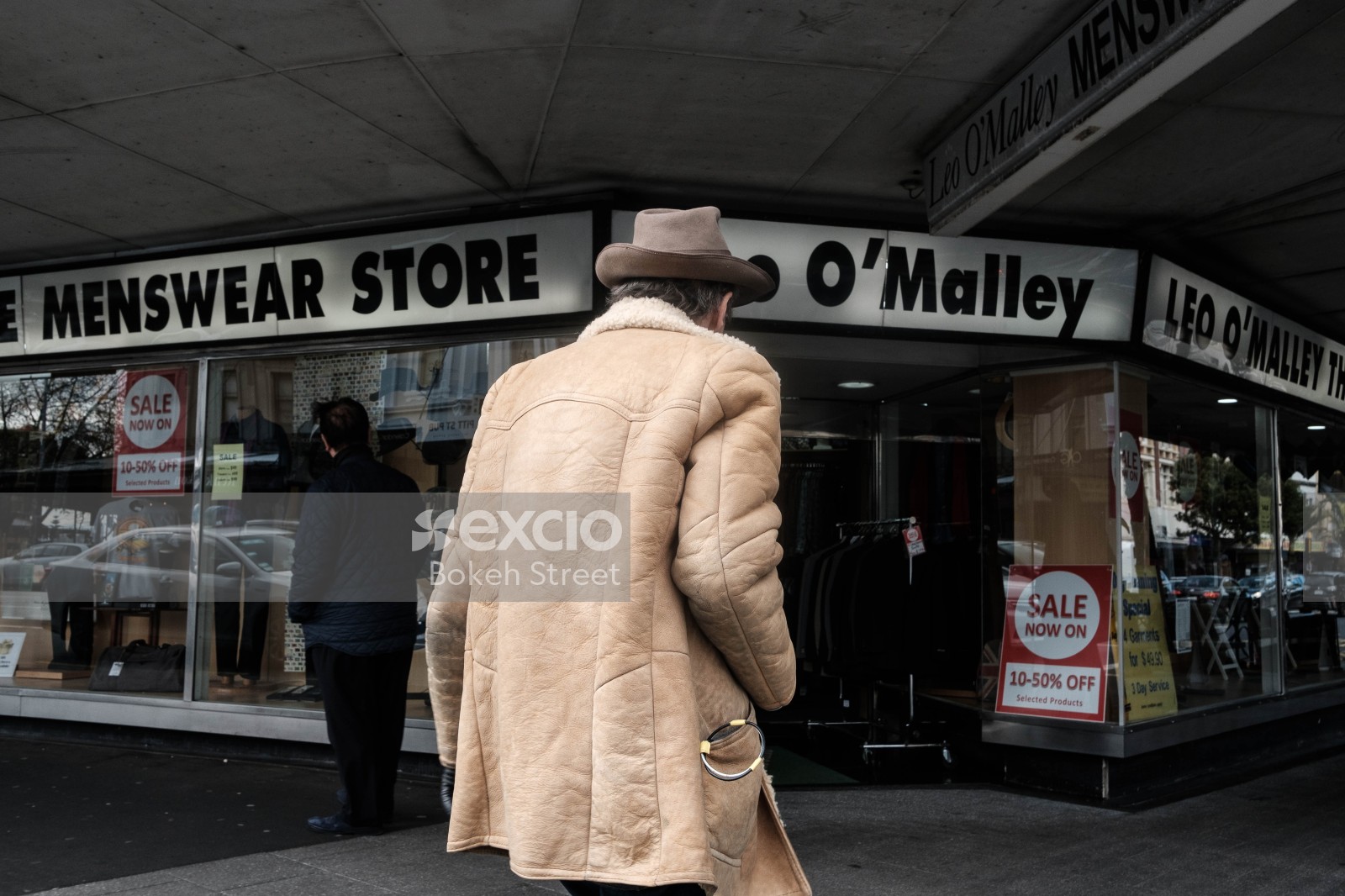Old man in coat and hat in front of shops at Ponsonby street